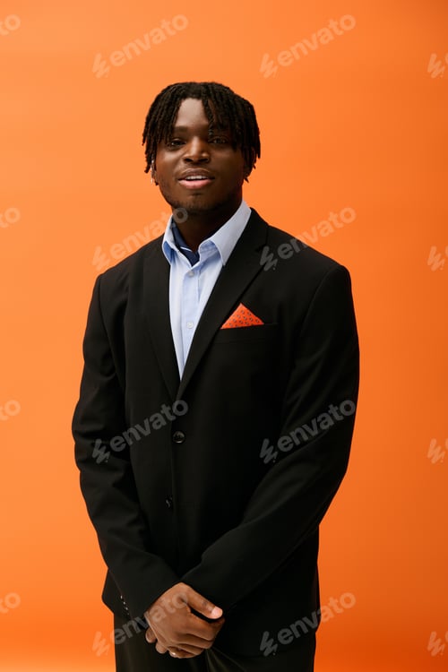 Preview: Stylish young man poses confidently against an orange backdrop while dressed elegantly