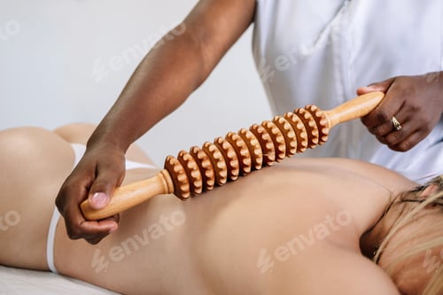 Preview: Crop masseur massaging back of unrecognizable female customer with wooden instrument in salon