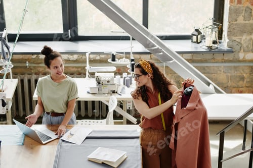 Preview: Happy young designer of fashion showing her colleague new models