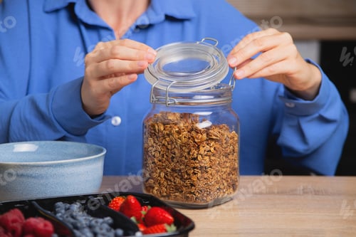 Preview: Granola in glass jar. Woman prepares quick breakfast.