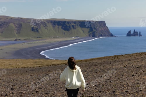 Preview: A girl running along a cliff with a view of Vik beach in Iceland.