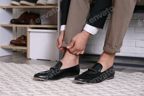 Preview: Man with stylish shoes sitting near shelving unit in hallway, closeup