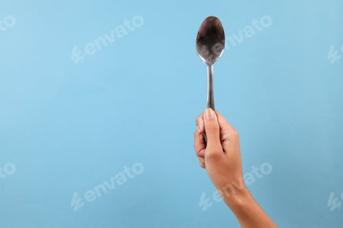 Preview: Hand Holding Spoon Against Blue Background