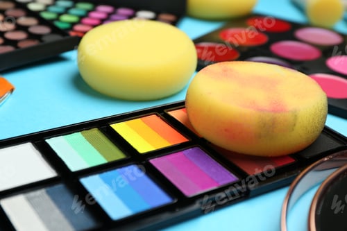 Preview: Bright face paints and sponges on light blue background, closeup