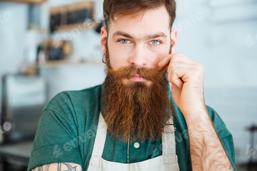 Preview: Handsome man with beard in white apron touching his moustache