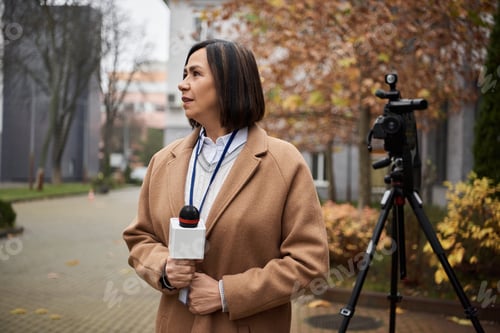 Preview: A multiracial female journalist in a beige coat reports news in a tranquil outdoor setting