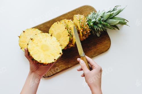 Preview: top view of person cutting fresh pineapple on wooden board, isolated on white