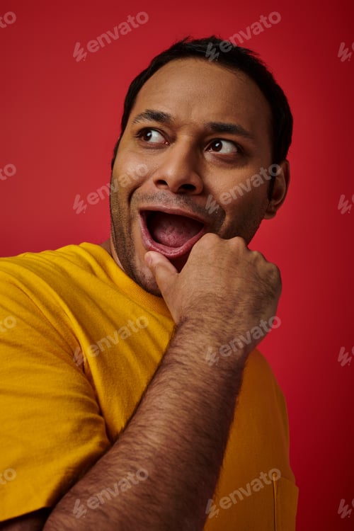 Preview: wow expression, amazed indian man in yellow t-shirt looking away with open mouth on red background