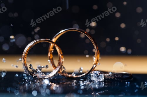 Preview: gold wedding rings for newlyweds on a wedding day on a black background with water drops. Jewelry