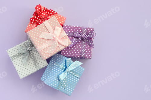 Preview: Pile of a small colored gift boxes with ribbons lies on a violet background. Minimalism flat lay