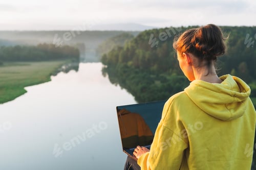 Preview: Young woman girl traveler freelancer in yellow hoodie with opened laptop