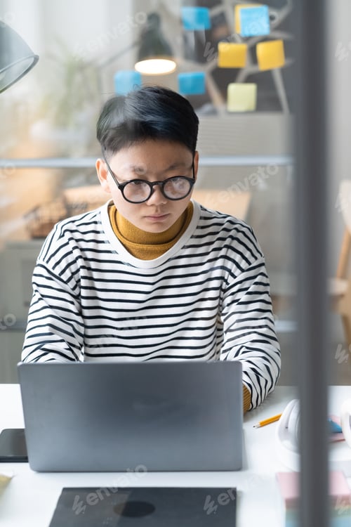Preview: Serious Asian businesswoman in eyeglasses concentrating on her online work on laptop at the