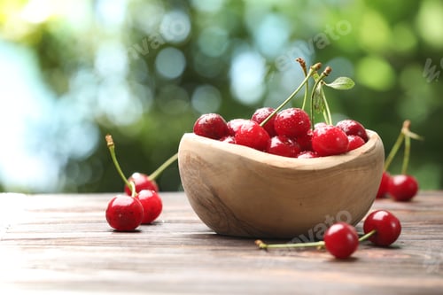 Preview: Fresh wet cherries in bowl on wooden table against blurred green background, closeup