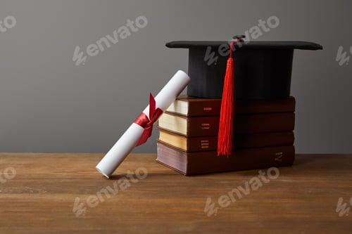 Preview: Diploma, academic cap and books on wooden surface isolated on grey