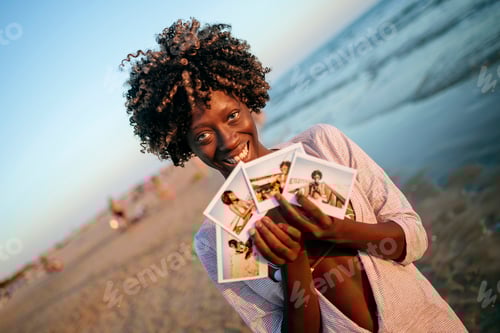 Preview: Woman showing printed photos on the beach at sunset