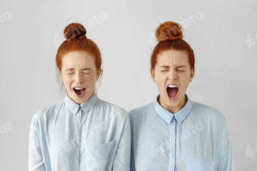 Preview: Indoor shot of furious young European women wearing identical hairstyles and formal wear, screaming