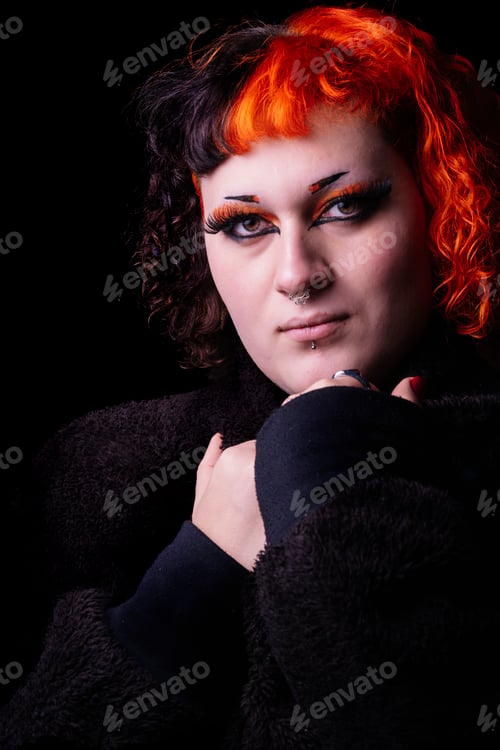 Preview: Portrait with black background of a young transgender woman with dyed orange hair.