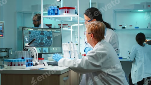 Preview: Team of scientist discussing and typing on pc late at night