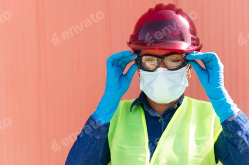 Preview: Hispanic heavy industry worker wearing protective mask and putting on safety goggles