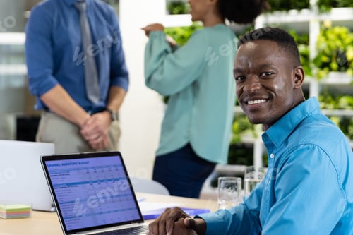 Preview: Portrait of happy african american businessman with laptop and diverse colleagues in modern office