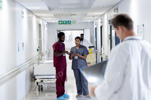 Preview: Diverse male and female doctor in scrubs looking at tablet talking in busy hospital corridor