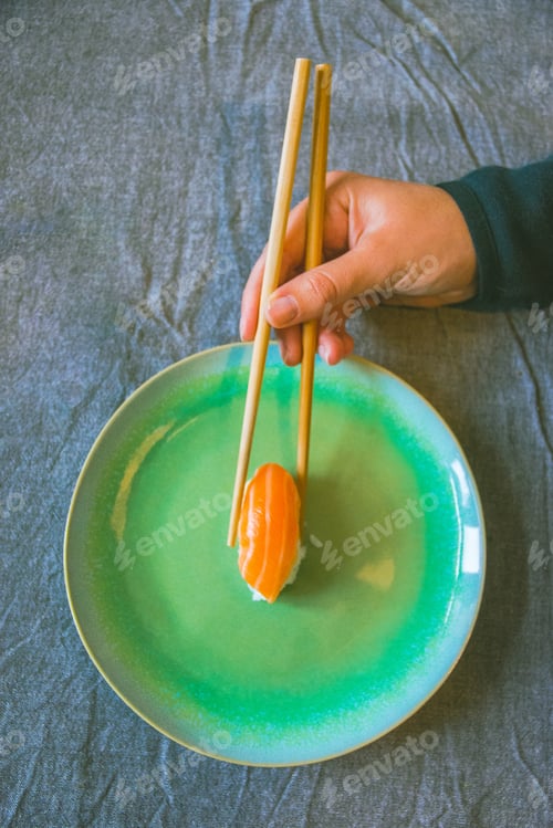 Preview: human hands with chopsticks eating sushi salmon fresh food green plate