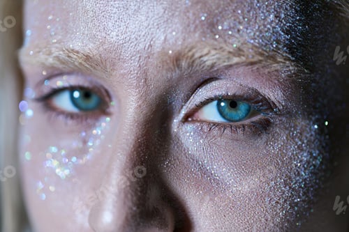 Preview: close up of beautiful female model with highlighter on her face and green eyes looking at camera