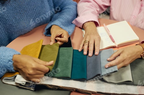 Preview: Hands of Two Female Designers Selecting Color on Fabric Samples while Sitting at Table