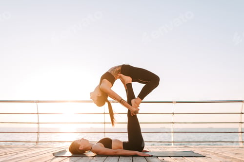 Preview: Two cool ladies in black sporty tops and leggings training yoga poses by the sea