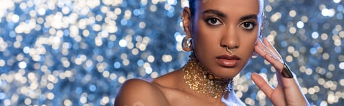 Preview: Trendy african american model in golden accessories on sparkling blue background, banner