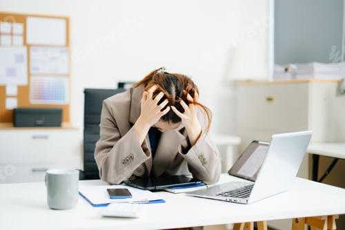 Visualização: Young woman overwhelmed and exhausted at her desk in modern office. Struggling with stress,