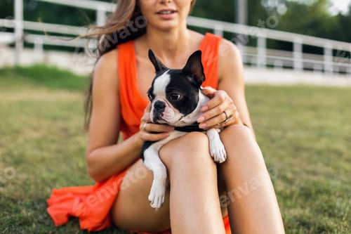 Preview: young happy smiling woman in orange dress having fun playing with dog in park