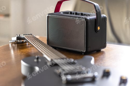 Preview: Black electric guitar and speaker on a wooden table.