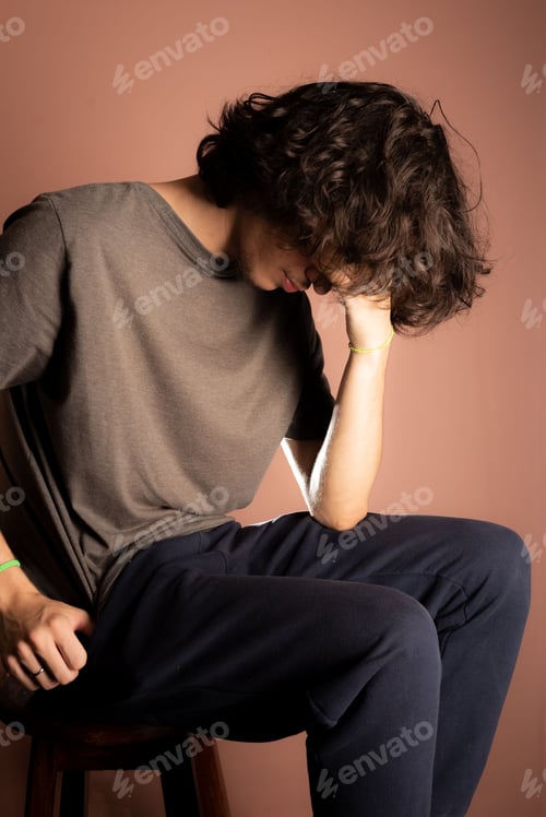 Preview: Caucasian adult man sits and displaying a feeling of distress as he rests his hand on his face