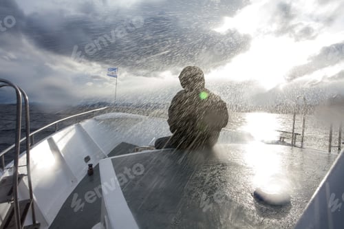 Preview: Person in waterproofs sitting in front of boat sailing in rain storm, Ushuaia, Tierra del Fuego,
