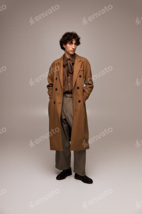 Preview: Stylish young man showcases modern fashion in a warm brown coat on a minimalist background