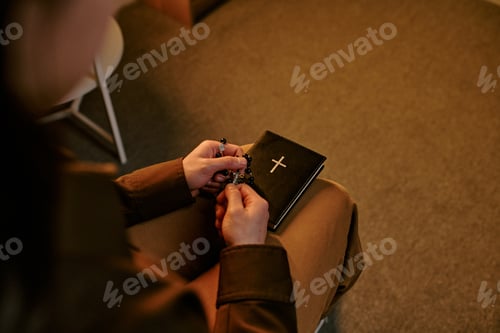 Preview: Young Adult Woman Praying with Rosary and Bible Indoors