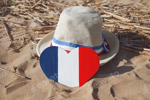 Preview: wooden heart straw hat with ribbon with colors of flag France blue white red in golden sand on beach