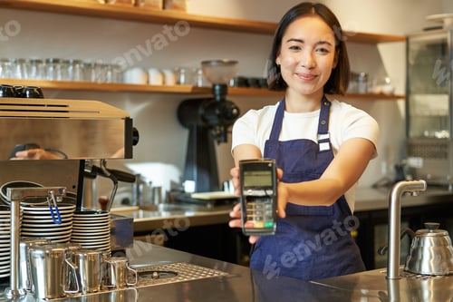 Preview: Smiling asian barista, coffee shop staff gives you credit card machine, processing payment with POS