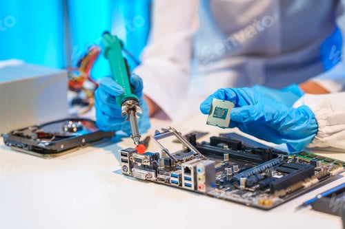 Preview: Close-up of a technician wearing gloves soldering electronic components at a desk in an office