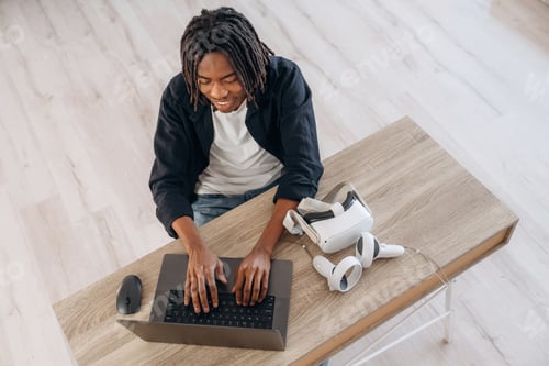 Preview: User is with headset. Young man is sitting by table with laptop and virtual reality glasses