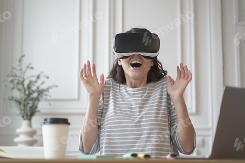 Preview: Excited entrepreneur lady tests virtual reality technology wearing VR glasses sitting at home office