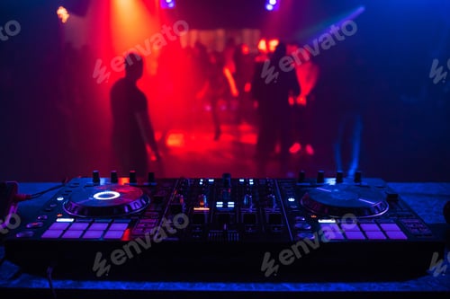 Preview: DJ console for mixing music with blurry people dancing at a nightclub party