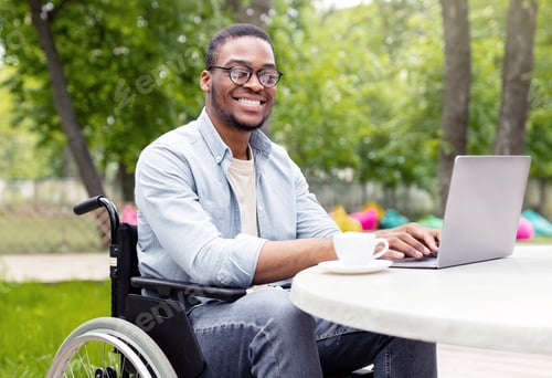 Preview: Joyful impaired black guy in wheelchair working on laptop at cafe in urban park, having business