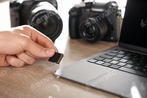 Preview: Man inserting SD memory card into laptop at wooden table indoors, closeup