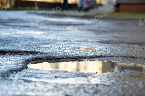 Preview: Close up of a road in very bad condition with big potholes full of dirty rain water pools