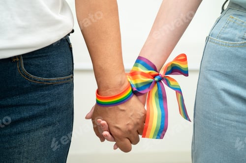 Preview: Asian LGBT couple woman holding hand wearing rainbow wristband.