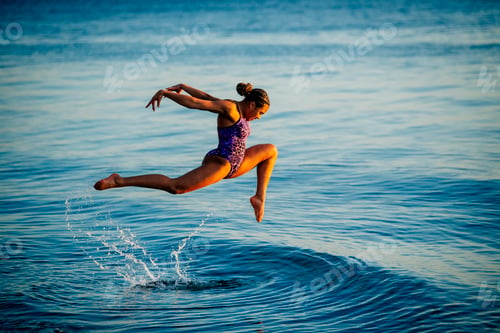 Preview: Woman in purple swimwear joyfully leaps above the water at the beach during sunset, USA