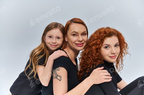 Preview: three generations concept, happy redhead family smiling and looking at camera on grey backdrop