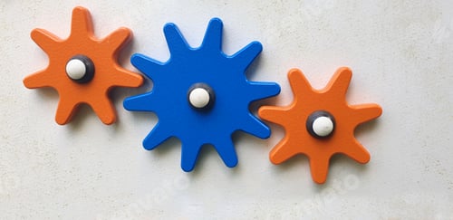 Preview: colored wooden cogwheels on white board